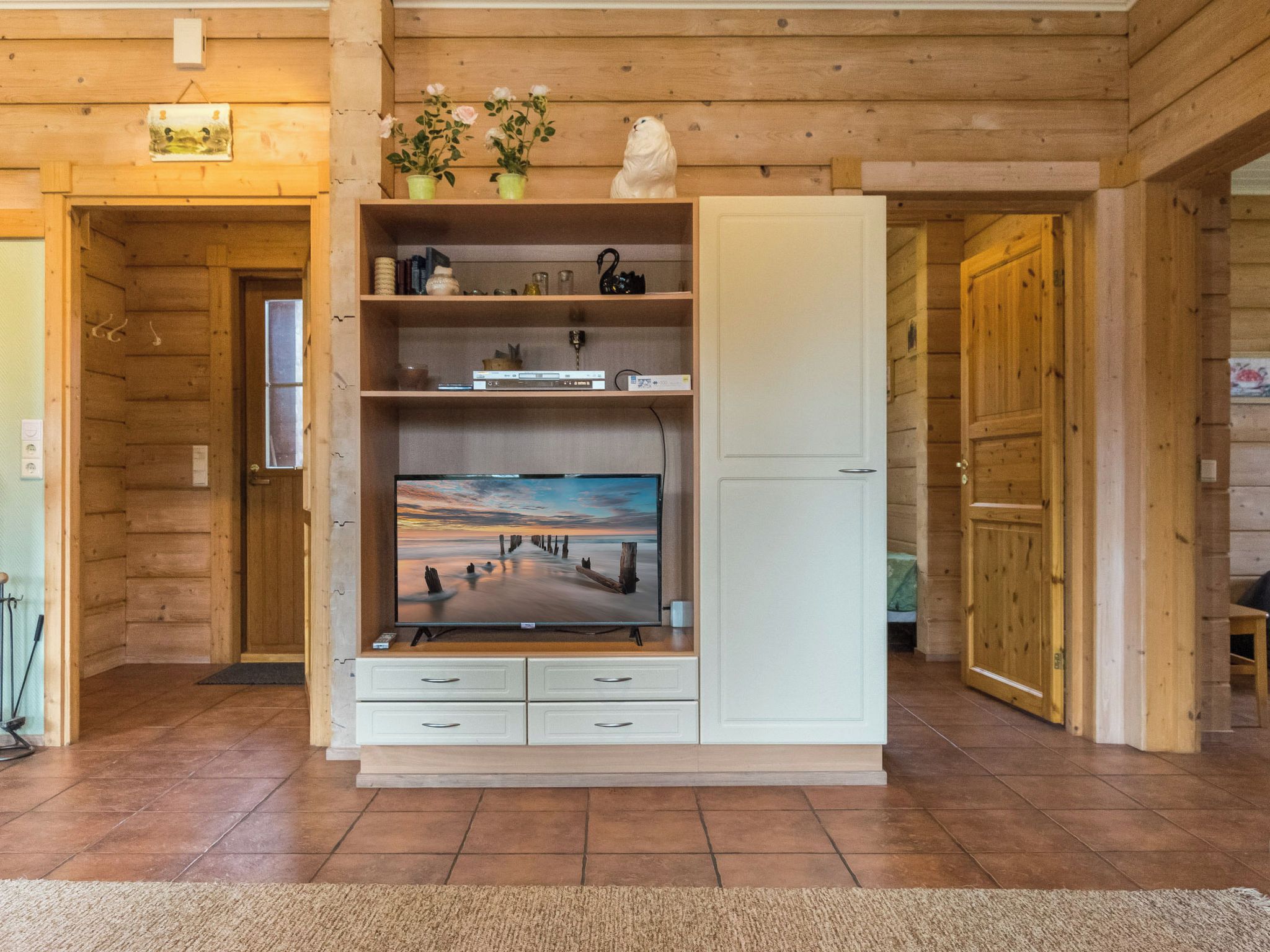 Un interior de madera con un televisor sobre un mueble, una puerta y una repisa con objetos decorativos.