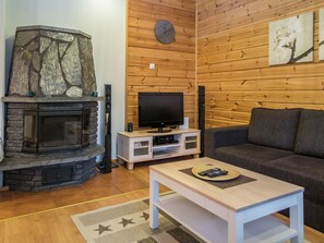 A living room with a stone fireplace, a flat-screen TV, a sofa, and a coffee table. - Tintintupa by Interhome (Nilsiä)