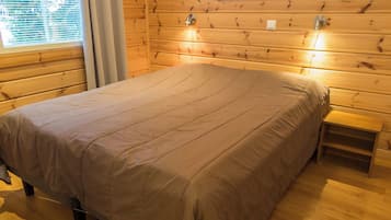 Ein Zimmer mit Holzwänden, einem Bett, einem Nachttisch und einem Fenster mit Jalousien.