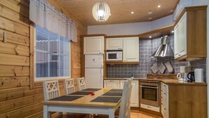 A compact kitchen with wooden walls, a dining table with chairs, a refrigerator, a microwave, a stove, and a sink. - Tintintupa by Interhome (Nilsiä)