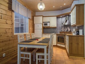A compact kitchen with wooden cabinets, a microwave, an oven, and a dining area with a table and chairs. - Tintintupa by Interhome (Nilsiä)