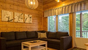 A cozy wooden cabin interior with a dark-colored sofa, a small white coffee table, and a large window with curtains. - Tintintupa by Interhome (Nilsiä)