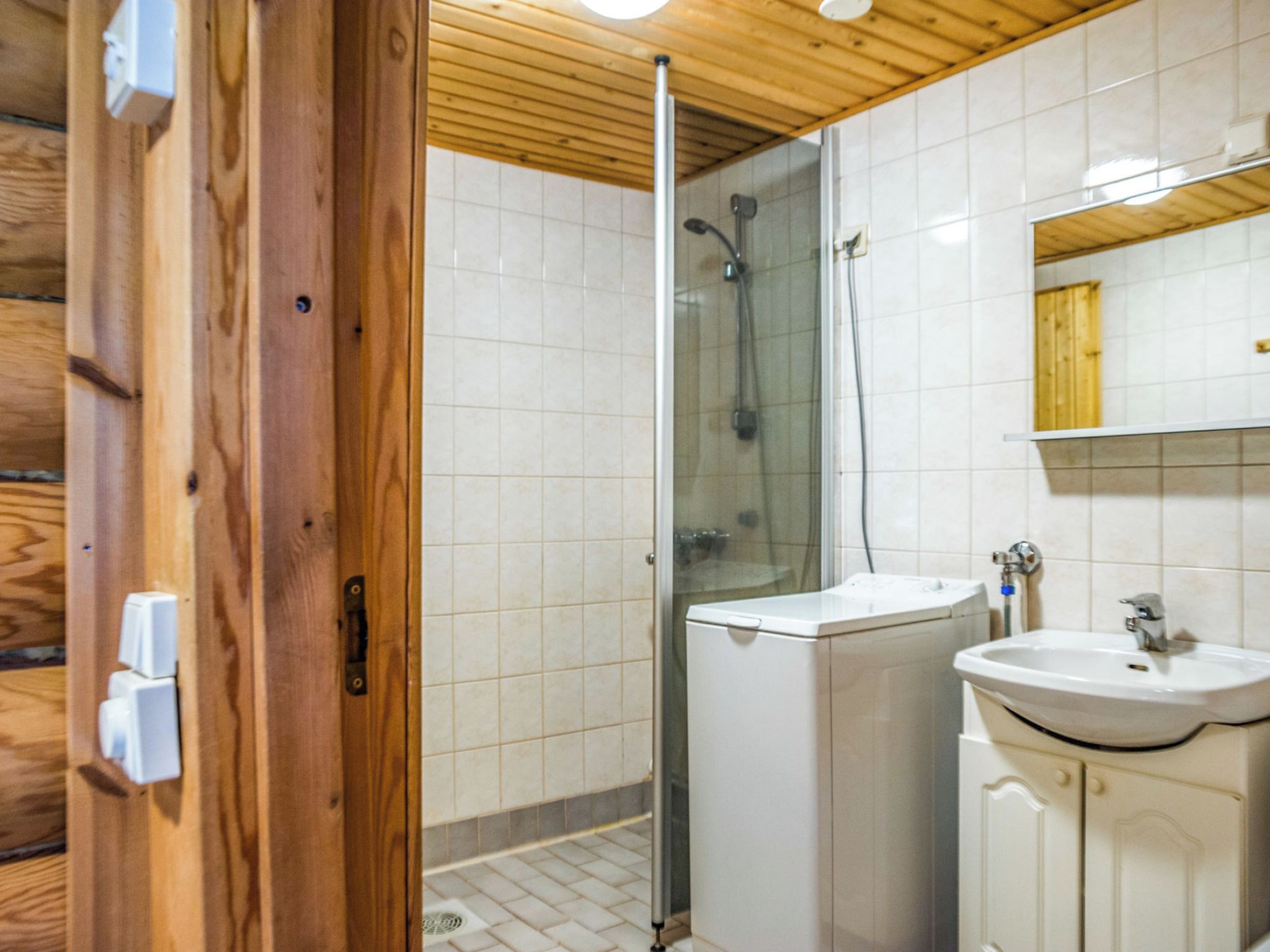 A wooden cabin bathroom with a shower, sink, and mirror.