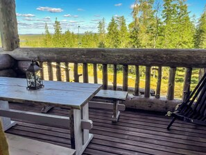 An outdoor deck with a wooden table and benches, overlooking a forested area. - Alte ruka by Interhome (Kuusamo)