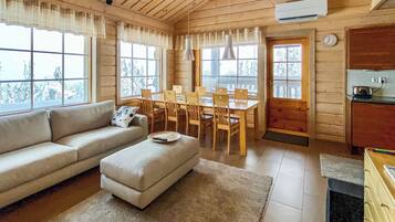 L’intérieur chaleureux d’un chalet comprend un canapé, un pouf, une table à manger, des chaises et un coin cuisine.
