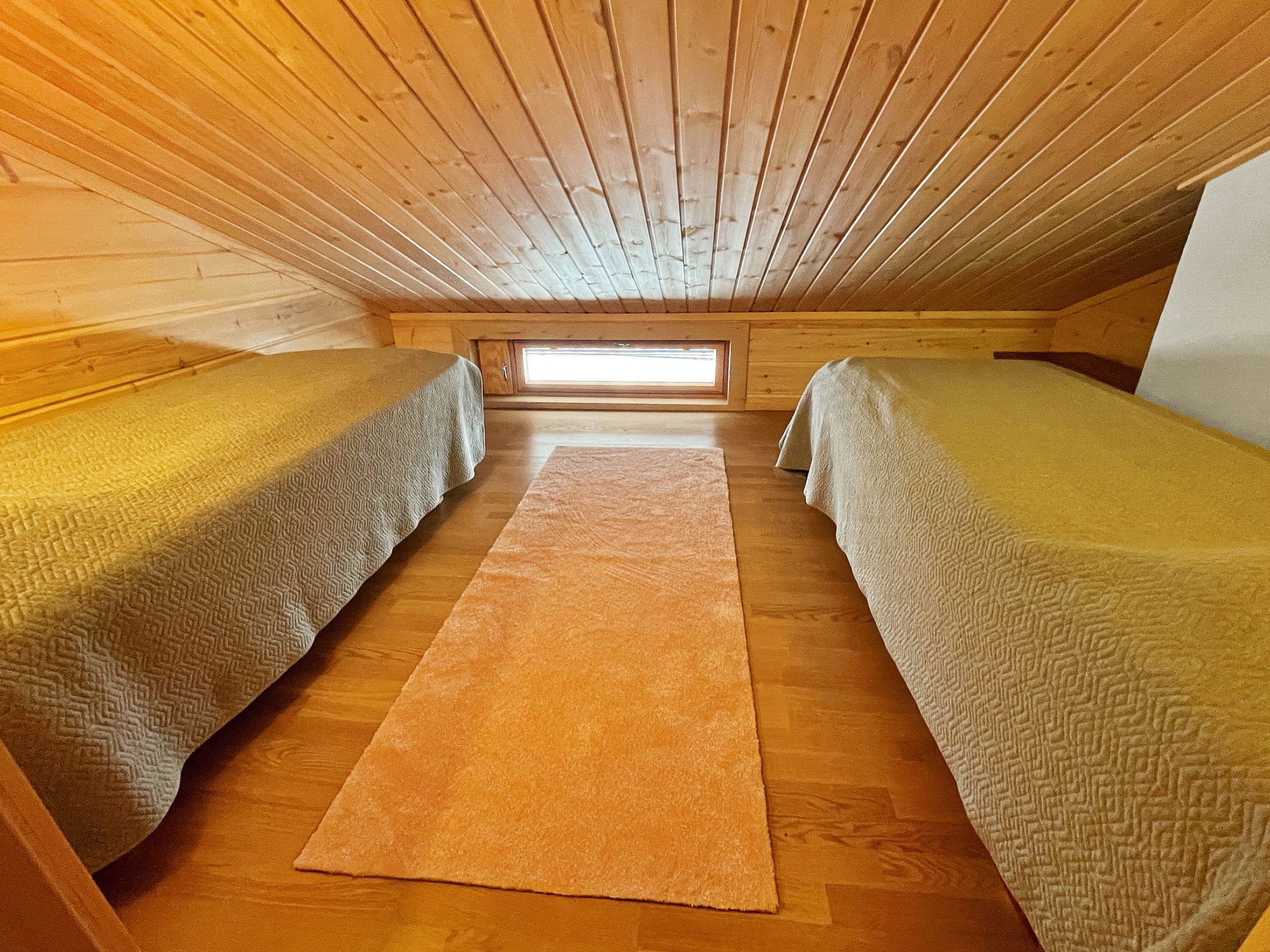A small, cozy attic bedroom with two single beds, a central rug, and a skylight.