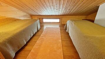 Une petite chambre mansardée, chaleureuse et accueillante, avec deux lits simples, un tapis au centre et une lucarne.