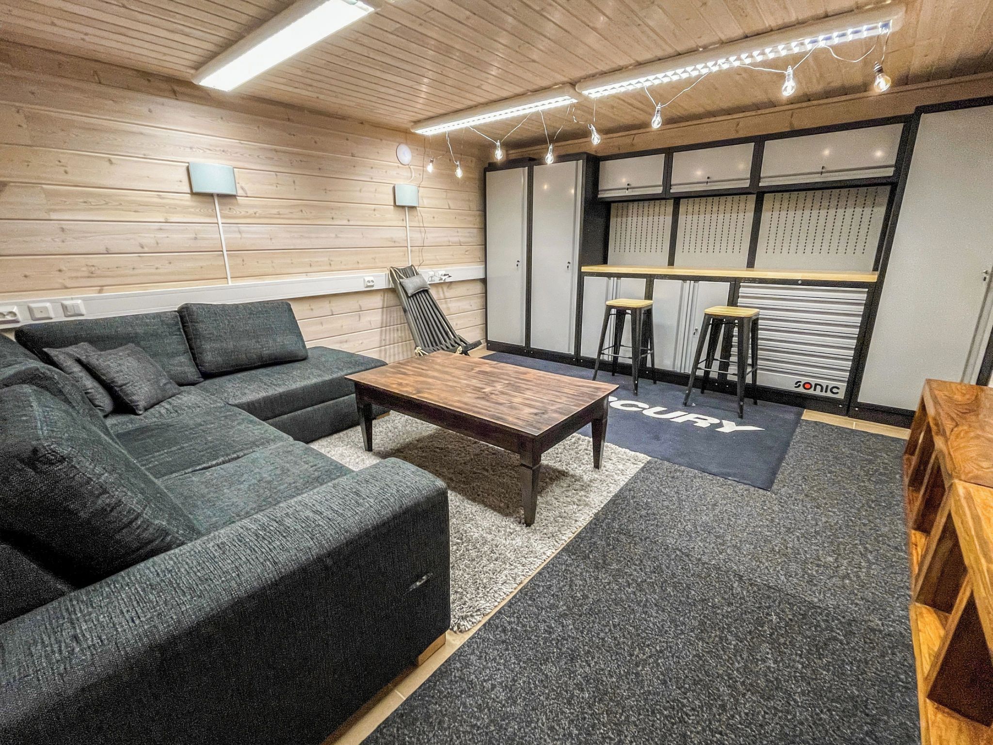 Un espace de détente moderne comprenant un canapé d’angle, une table basse en bois et des tabourets de bar.