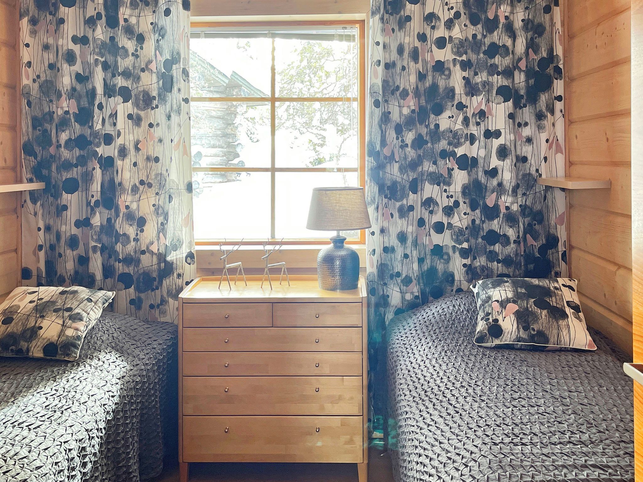 Een kamer met twee bedden, een houten dressoir en een raam met gordijnen.