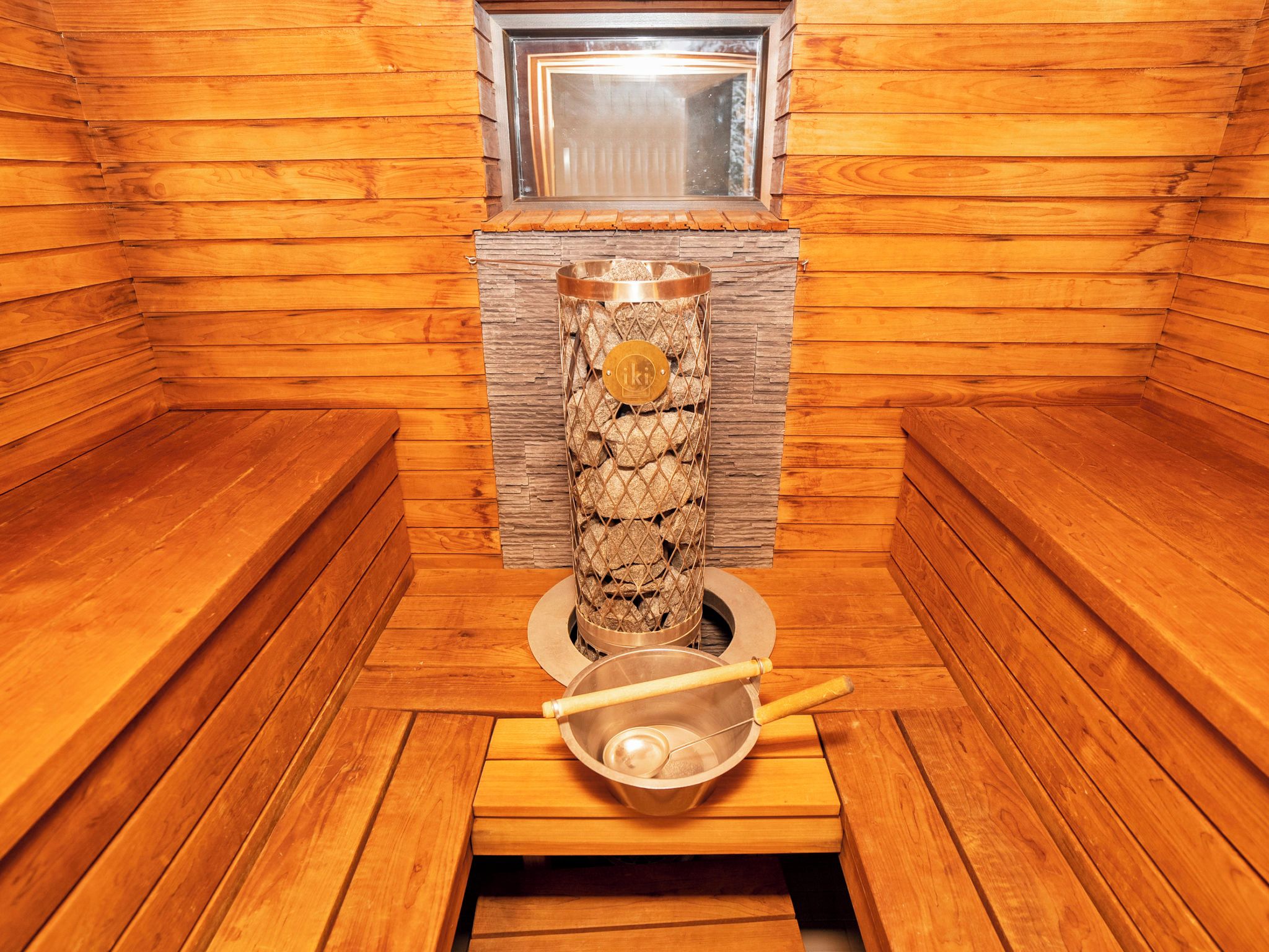 A sauna room with wooden walls, a stone wall, and a metal container with a handle.