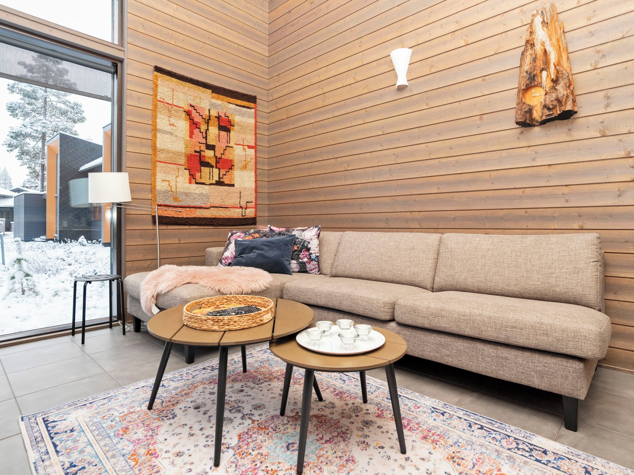 A modern living room with a sofa, two coffee tables, a rug, and a wall tapestry.