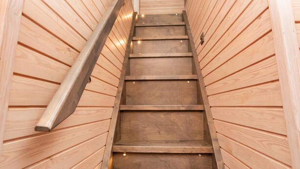 A wooden staircase with a metal handrail, leading upwards.