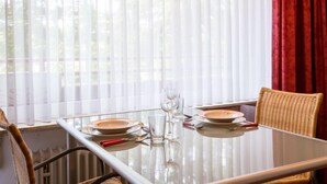 A dining table set for two with white plates and clear glasses, positioned near a window with sheer curtains. - Wanderlust (B212) by Interhome (Lahnstein (Koblenz))