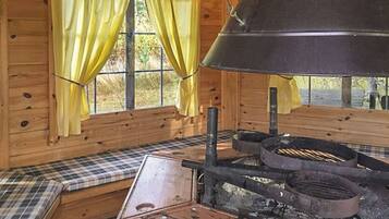 A rustic cabin interior with a large stove, plaid-patterned bench, and yellow curtains.