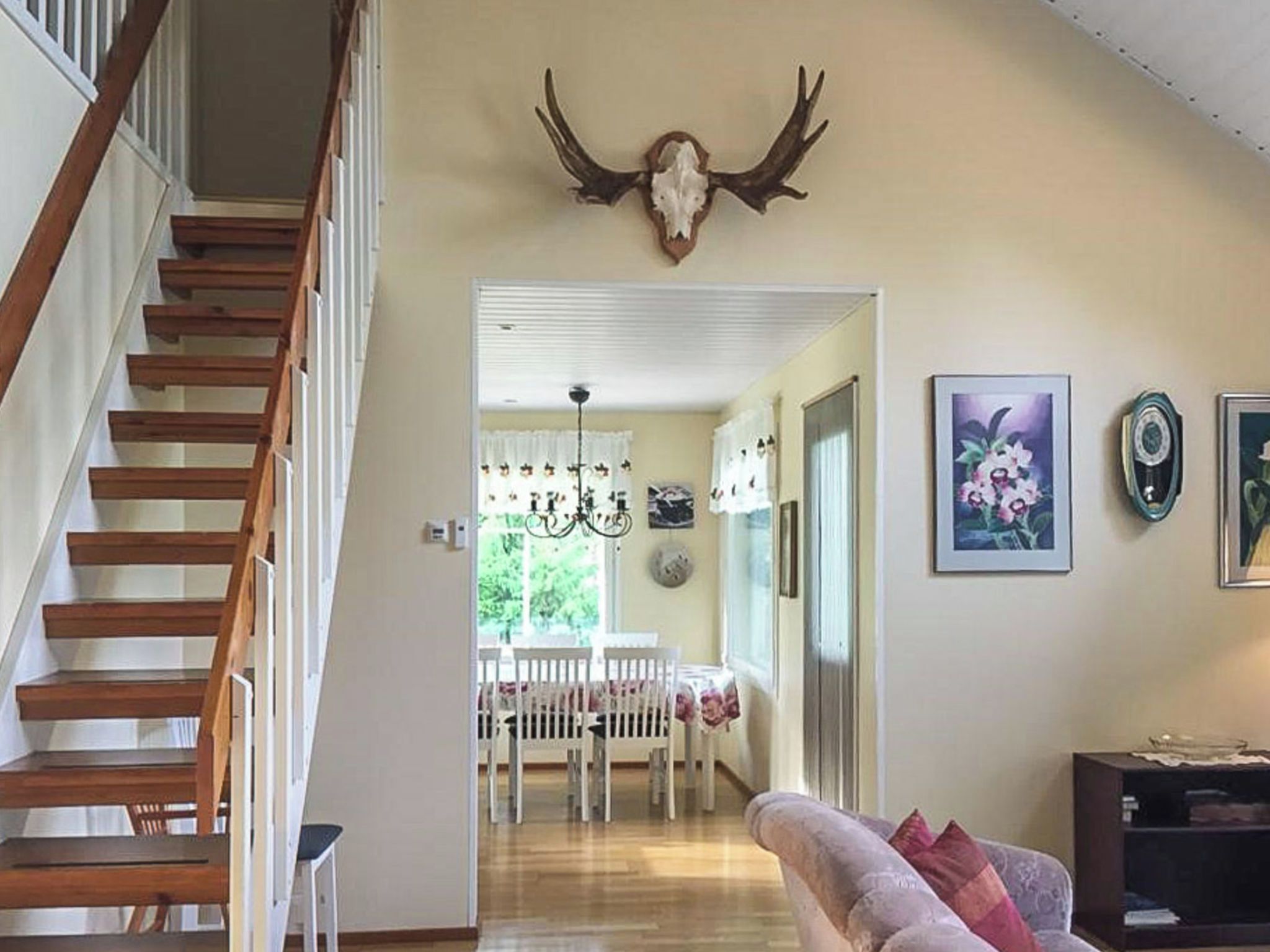 A staircase leading to a dining area with a chandelier, a wall-mounted deer skull, and framed artwork.
