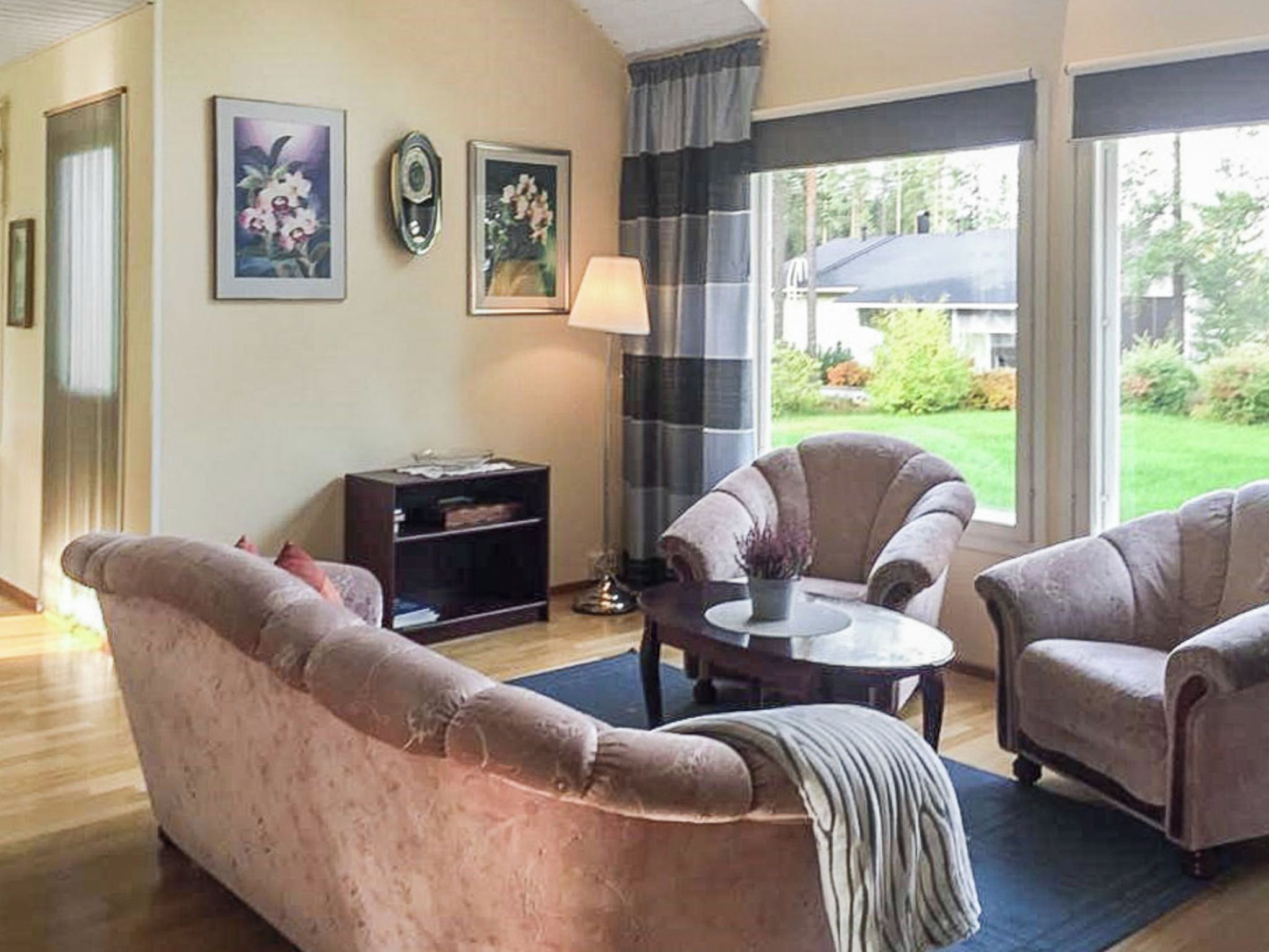 A living room with a sofa, armchairs, a coffee table, and a lamp. There are two framed pictures on the wall.