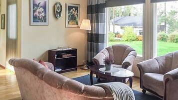 A living room with a sofa, armchairs, a coffee table, and a lamp. There are two framed pictures on the wall.