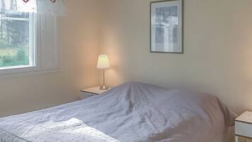 A bedroom with a bed, a nightstand, a lamp, a window with curtains, and a framed picture on the wall.
