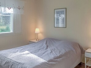 A bedroom with a bed, a nightstand, a lamp, a window with curtains, and a framed picture on the wall.
