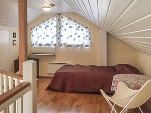 A bedroom with a sloped ceiling, a bed, a chair, and a window with floral curtains.