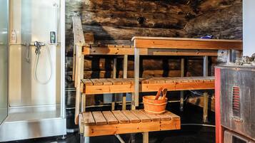 A rustic cabin interior with a wooden bench, a metal sink, and a refrigerator.