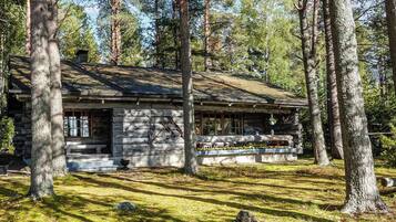 A log cabin with a porch, surrounded by trees.