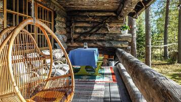 A rustic wooden cabin with a hanging chair, a table with a blue tablecloth, and a log railing.