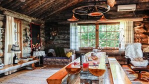 Interior rústico de una cabaña con una larga mesa de madera, bancos y una zona de estar acogedora.