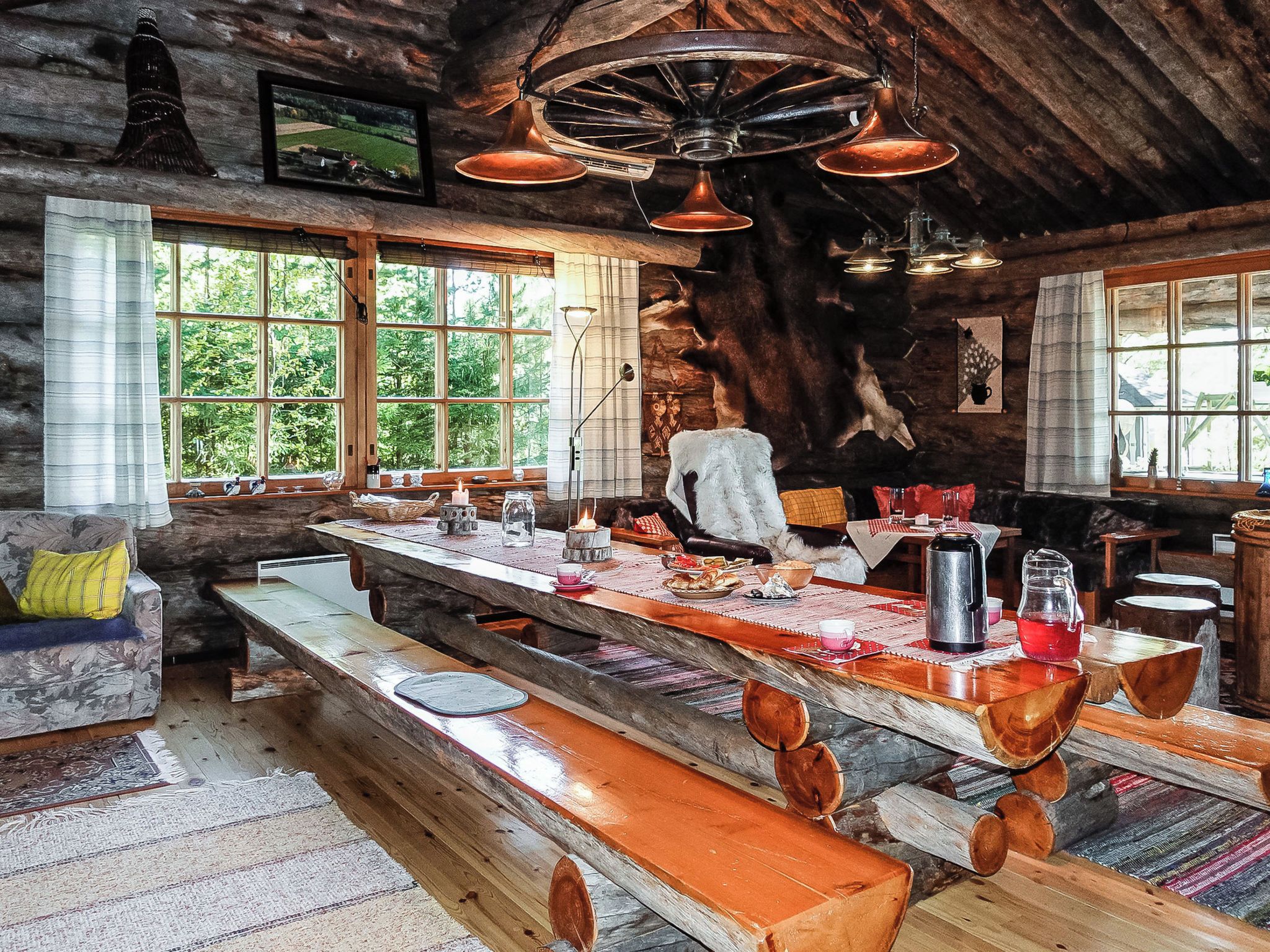 A rustic cabin interior with a large wooden dining table, benches, and a stone fireplace.