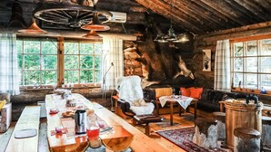 Interior rústico de una cabaña con una mesa de comedor de madera, un sofá de cuero y un ventanal con vistas a la vegetación.