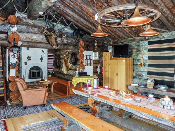 A rustic interior with a wooden ceiling, a fireplace, a dining area with a table and chairs, and a bar with a counter.