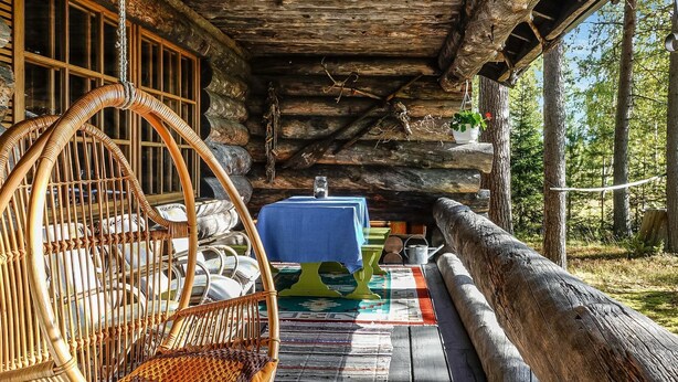 Una cabaña de madera rústica con una mecedora, una mesa con mantel azul y una terraza de madera.