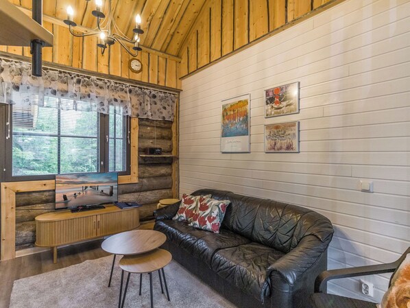 L’intérieur d’un chalet accueillant, avec un plafond en bois, un canapé en cuir, une petite table et un téléviseur.