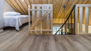 A bedroom with a sloped ceiling, wooden beams, a bed with a white bedspread, and a window with a view of a stone wall. - Kantapää d2 by Interhome (Sodankylä)