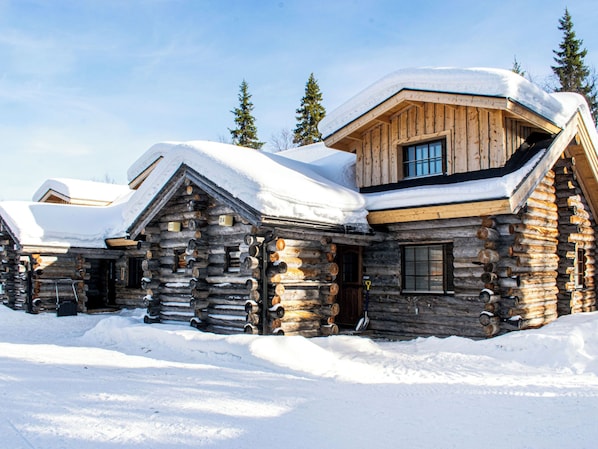 Eine Blockhütte mit schneebedecktem Dach, Holzwänden und einem großen Fenster.