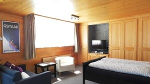 A wooden-paneled room with a bed, a TV, a small table, and a sofa. - Bijou Arnensee by Interhome (Feutersoey)
