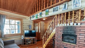 Ein gemütliches Blockhaus-Interieur mit einer Holztreppe, einem Kamin, einem Fernseher und einem Sofa.