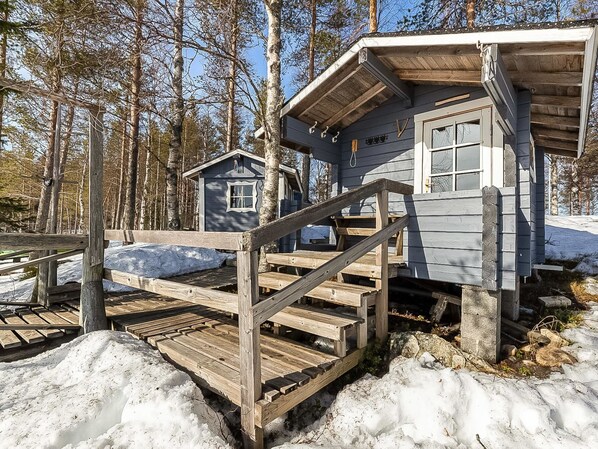 Eine Holzhütte mit einer Holztreppe, die zu einer Terrasse führt, umgeben von Schnee und Bäumen.