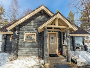 Une cabane en rondins avec un porche à l’avant, une porte ornée d’une guirlande et une fenêtre avec un cadre décoratif.
