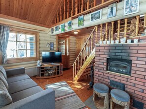 Un intérieur de chalet chaleureux avec un escalier en bois, une cheminée, un téléviseur et un coin salon confortable.