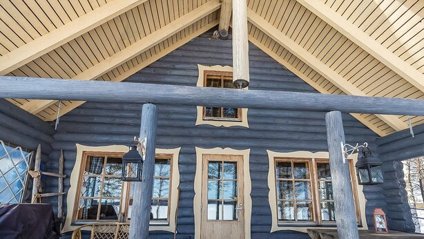 Eine Blockhütte mit einem steilen Satteldach, mehreren Fenstern mit Holzrahmen und einer Veranda aus gestapelten Baumstämmen.