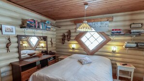 Ein gemütliches Schlafzimmer in einer Blockhütte mit einem großen Bett, einem Holzkopfschild, einem Schminktisch, einem Spiegel und Bücherregalen.