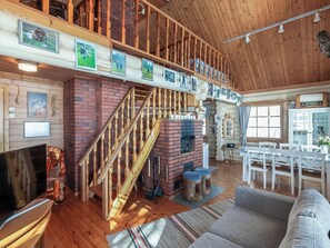 A spacious loft-style living area with a wooden staircase, a fireplace, and a dining area with white furniture.