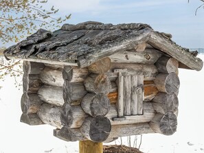 Un nichoir à oiseaux de style cabane en rondins, doté d’un toit incliné et d’une porte en bois.