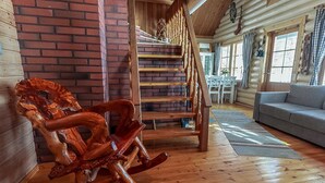 Ein rustikales Blockhaus-Interieur mit einem Schaukelstuhl aus Holz, einer Holztreppe und einem Sofa.