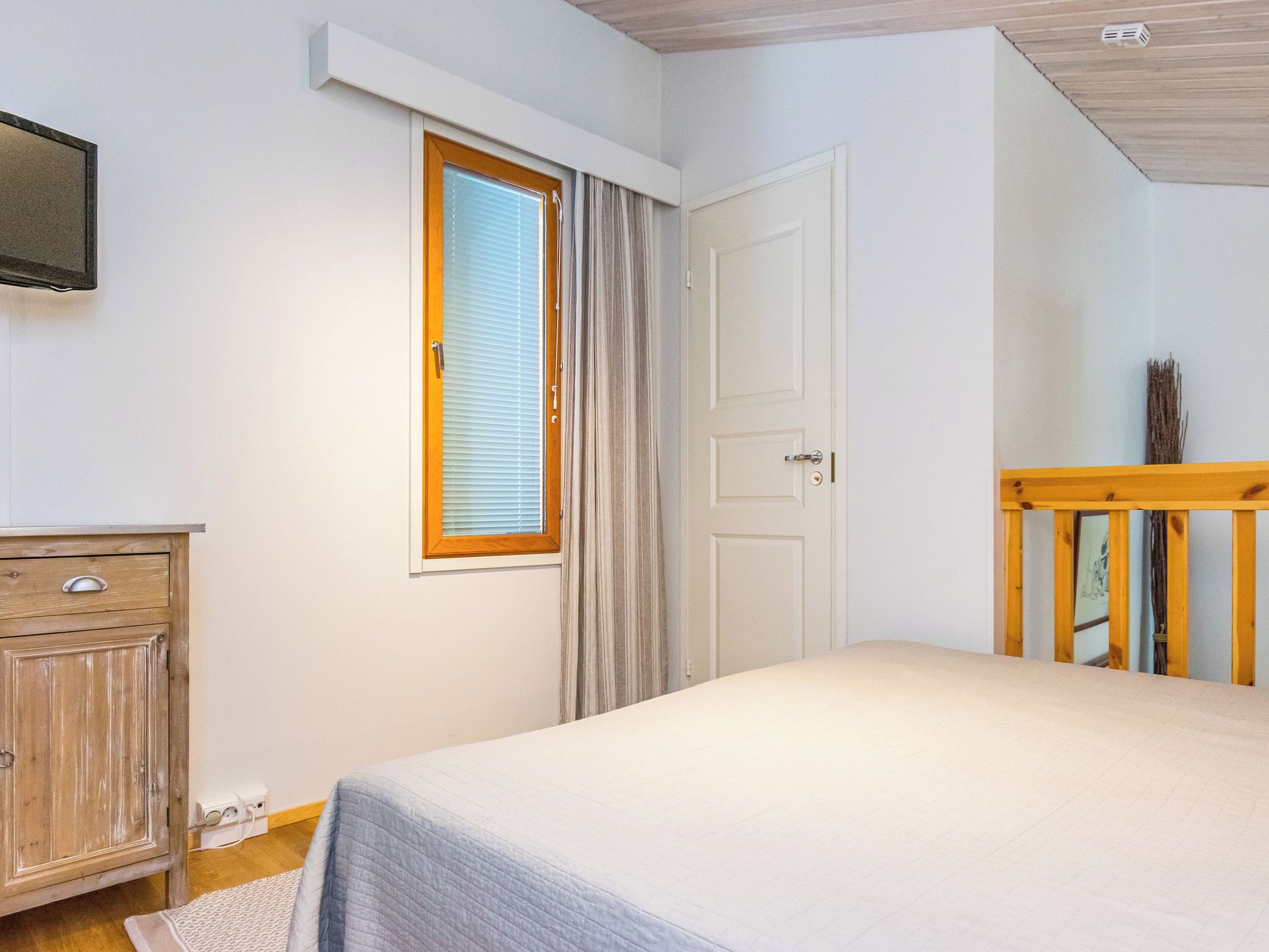 Un dormitorio con cama, cómoda de madera, ventana con cortinas y puerta.