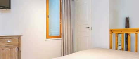 Un dormitorio con cama, cómoda de madera, ventana con cortinas y puerta.