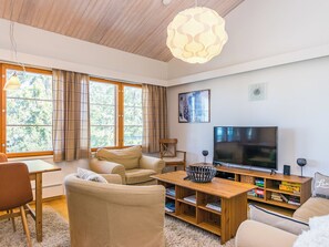 Una sala de estar con un sofá, un televisor, una mesa de centro de madera y una estantería.