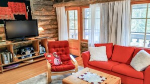Interior acogedor de una cabaña de troncos con un sofá rojo, un sillón rojo, una mesa de centro de madera y un televisor sobre un mueble de madera.