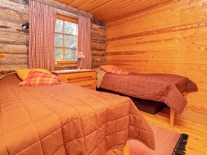 A cabin-style room with two beds, a window with curtains, and a wooden floor. - Karhunpesä by Interhome (Kuusamo)